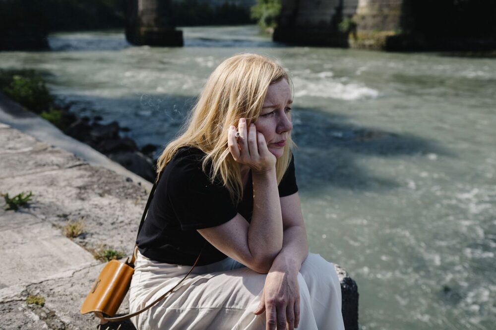 Ingeborg Bachmann (Sandra Hüller) sitzt, nachdenklich auf das Wasser schauend und rauchend, am Ufer des Tiber in Rom.